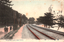 This coloured card shows a double-track railway curving through a wooded coastal landscape, with several people walking beside the railway. On the card is printed “Ichinotani, Suma (near Kobe).” and “須磨 一ノ谷”. Japanese translation:
須磨 — “Suma.”
一ノ谷 — “Ichinotani” (Ichi-no-Tani).
Together: “Ichinotani, Suma.”