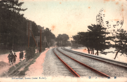 This coloured card shows a double-track railway curving through a wooded coastal landscape, with several people walking beside the railway. On the card is printed “Ichinotani, Suma (near Kobe).” and “須磨 一ノ谷”. Japanese translation:
須磨 — “Suma.”
一ノ谷 — “Ichinotani” (Ichi-no-Tani).
Together: “Ichinotani, Suma.”