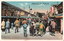 This coloured card shows a crowded shopping street at Asakusa, with shops and signs on both sides. On the card is printed “Nakamise at Asakusa.” There is no separate printed Japanese caption along the border. A vertical shop sign at the right reads “寿司”, meaning “sushi.”