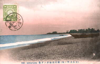 This coloured card shows a coastal beach with boats, calm water and a wooded shoreline. On the card is printed “THE. KOKUFUZU.” and “（日本名所ノ内）國府津海岸ノ夕暮”. Japanese translation:
（日本名所ノ内）國府津海岸ノ夕暮 — “(Among the famous sights of Japan) Evening at the Kōzu coast.”
日本名所ノ内 — “Among the famous sights of Japan”
國府津 — Kōzu, in the older character form; modern 国府津
海岸 — coast / seashore
ノ夕暮 — “at evening” / “evening scene”