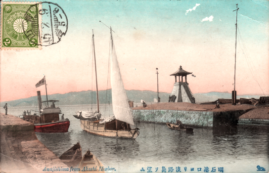 This coloured card shows a harbour entrance with several boats and a watchtower, looking across the water toward Awaji Island. On the card is printed “Awajishima from Akashi Harbor.” and “明石港口ヨリ淡路島ヲ望ム”. Japanese translation: 明石港口ヨリ淡路島ヲ望ム — “View of Awaji Island from the entrance of Akashi Harbor.”