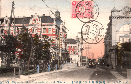 This coloured card shows a Tokyo streetscape with large commercial buildings, a motor car and utility poles. On the card is printed “NO 571 Drygoods Stkre Mitsugoshi & Pank Mitsuwi” and “（東京名所）三越呉服店及び三井銀行”. Japanese translation:
（東京名所）三越呉服店及び三井銀行 — “(Famous sight of Tokyo) Mitsukoshi Dry Goods Store and Mitsui Bank.”
東京名所 — famous sight of Tokyo
三越呉服店 — Mitsukoshi dry goods / drapery store
及び — and
三井銀行 — Mitsui Bank
