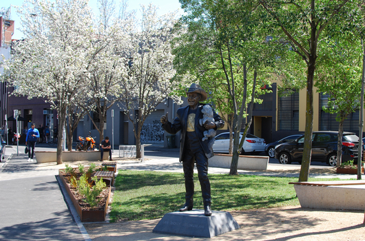 A larger-than-life bronze statue of a cheery man wearing installed at a park.