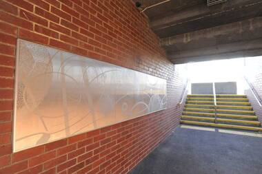 Metal panel artwork on red brick wall in an underground walkway.