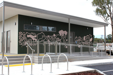 A sports pavilion painted dark green on one wall featuring bold outlines in dusty pink that depict various plants, trees, hills and buildings. 