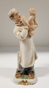 Sculpture - Porcelain figurine of a doctor holding a newborn baby
