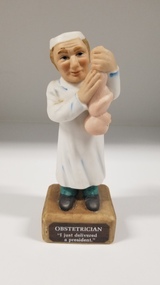 Sculpture - Porcelain figurine of an obstetrician holding a baby, Abbott, 1972