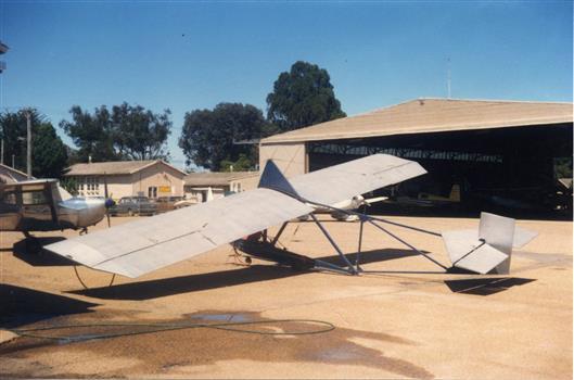 Silver and blue glider at rest in front of hangar