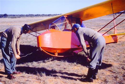 Orange glider in field attended by two men