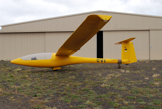 Yellow glider at rest in front of hangar
