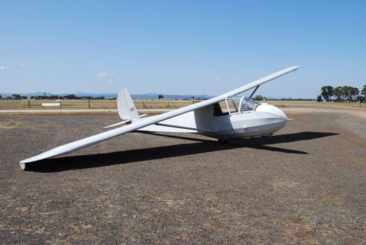 Light coloured glider at rest in open space - airfield in background
