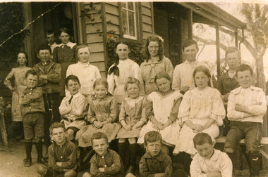 Twenty pupils (8 girls, 12 boys) in front of Teddywaddy State School No. 2064 a weather board building. In four rows.