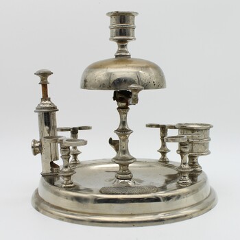 Silver stand to hold 8 pipes and pipe cleaner, A bell on top. Match striker plate and cigar cutter. Candle holder on top. Tarnished.