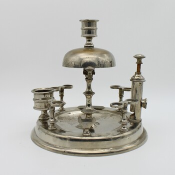 Silver stand to hold 8 pipes and pipe cleaner, A bell on top. Match striker plate and cigar cutter. Candle holder on top. Tarnished.