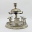 View from the side of the Pipe stand. Silver stand to hold 8 pipes and pipe cleaner, A bell on top. Match striker plate and cigar cutter. Candle holder on top. Tarnished.