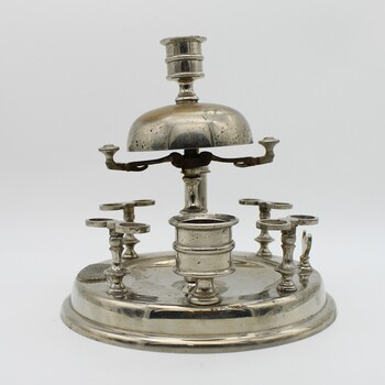 View from the side of the Pipe stand. Silver stand to hold 8 pipes and pipe cleaner, A bell on top. Match striker plate and cigar cutter. Candle holder on top. Tarnished.