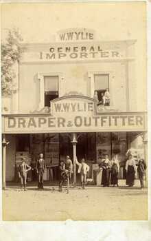 W. Wylie Store,  c.1890s. Nine people standing out front (store workers ), three others in the second story window, two of these are children. One person on a bicycle out front.