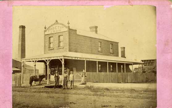 Procter and Son Butcher. Two men in butchers aprons, a woman and teenage child.  Front of shop is festooned with carcasses.