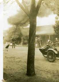 Petrol bowser fire. Onlookers include a dog and a man, three men standing together, and three other men on the rh side of the photo. A motorbike with a side car.