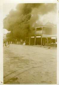 Petrol bowser fire c.1930. Thick smoke in coming from the front of the building a crowd of eight men are watching from the road.