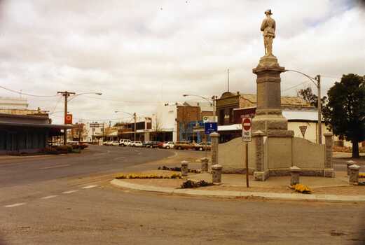 View of War Memorial looking east down High St. Back view of memorial. No entry sign. Lots of cars parked in front of the main street shops. 