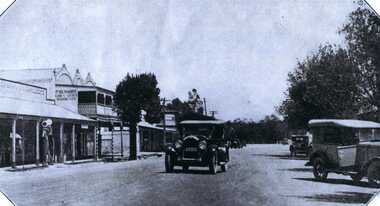 View looking down High Street, Charlton. Cars are passing. Store fronts in the main street. Sign reads "Richards - Ladies and Gents Hairdresser"