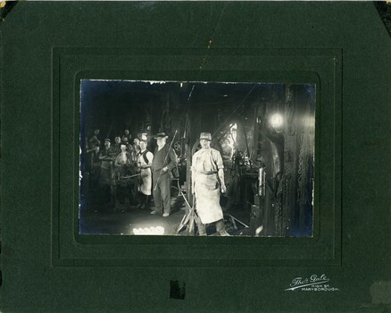 Group of nine workers standing in front of machinery inside Foundry.