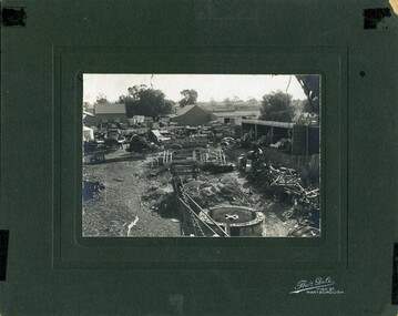 Foundry backyard showing farm machinery and implements. Three workmen in the yard. 