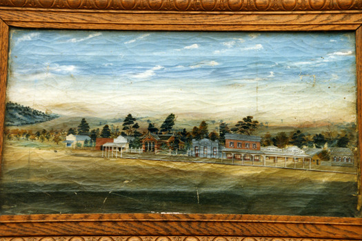 Framed painting of the east end, south side of High St Charlton. Shows 10 buildings; general store, etc and Tribune Office