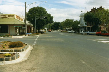 Garden beds in lower LH, road signs pointing to St Arnaud and to Mildura and Donald. North Central Panel Beaters on corner. Orange car driving west.