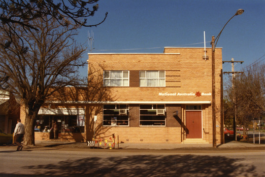 National Australia Bank. Two story building with white curtains in two upper storey windows. Entrance doors are shut. Man crossing High St on LH side of photo.
