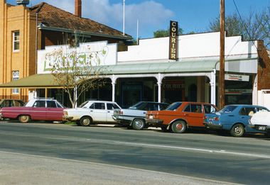 Two storey brick building. Seven cars of various colours parked in front.
