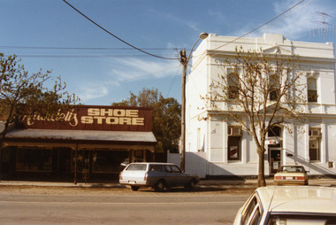 Shoe Store on the left and the two storey, white Westpac Bank on the right. Blue and white station wagon parked in front
