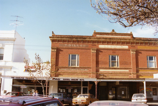 Two story, triple fronted red brick building. Cars parked in front. Signage reads THE CHARLTON PHARMACY and RUSSELL ENGLISH M.P.S. on verandah frontage. 
