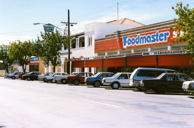 Foodmaster SUPERMARKET. Signage on the verandah reads C&H LICENCED SUPERMARKET, WOOL, HABERDASHERY. Red blinds down on verandah. Cars parked along the street.