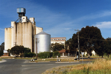 Charlton Flour Mill and silos. One large silver silo and three taller greyish concrete silos to the left. Three other cream coloured silos behind. 