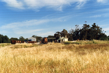 Railway Station. On the right, there is a small cream and green weatherboard building with a large verandah. There is a train engine and trucks in the middle of the photo.