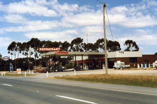 Roadhouse taken from the highway looking south east. A single storey building with large windows and large roof extending over the petrol pumps.