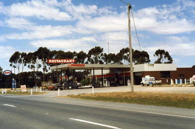 Roadhouse taken from the highway looking south east. A single storey building with large windows and large roof extending over the petrol pumps.
