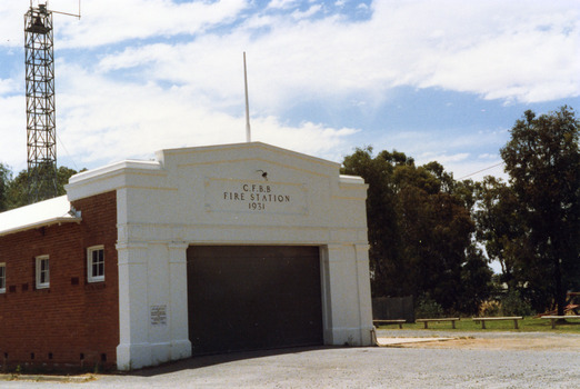 Fire Station. A single storey red brick building with a white frontage. A large entrance and three high high windows down the side. 