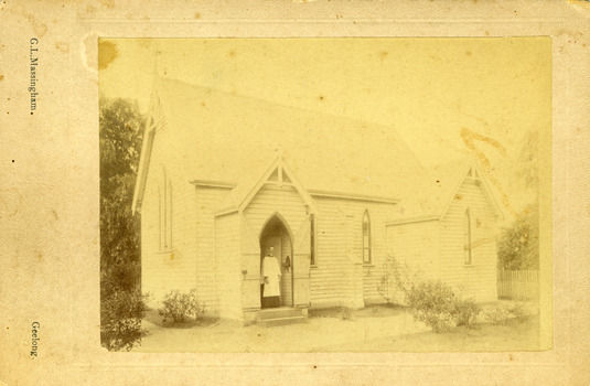 A cleric stands in the doorway to the weatherboard church.