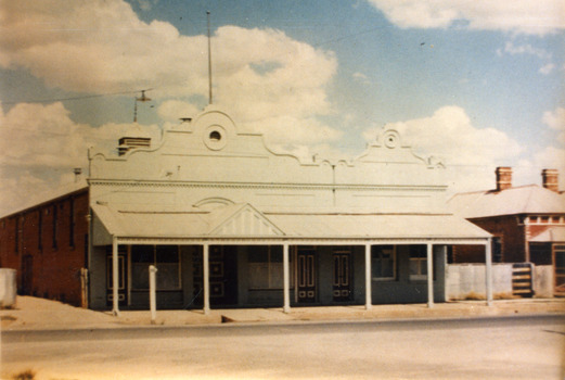 Single storey, triple fronted red brick building. The front of the building is painted. There are double doors for the main entrance and three single doors.