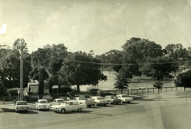 1973 flood at Gordon Park Charlton. 8 cars are lined up along road in front of park entrance. Flood waters have inundated the park.