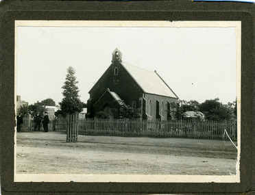 Brick church with a white picket fence. Three men stand to one side. Church has A.D. 1871  on the front