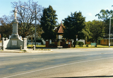 Granite War monument to the left, Brick rotunda in the center within Elliot Garden, Sign reads Elliot Gardens.