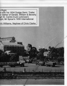 White wheat silo next to large flour mill. Trucks with wheat sacks in front.