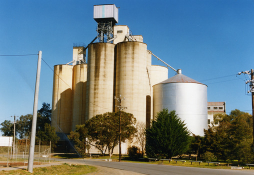 Several tall concrete wheat silos. A shorter metal wheat silo to the right.