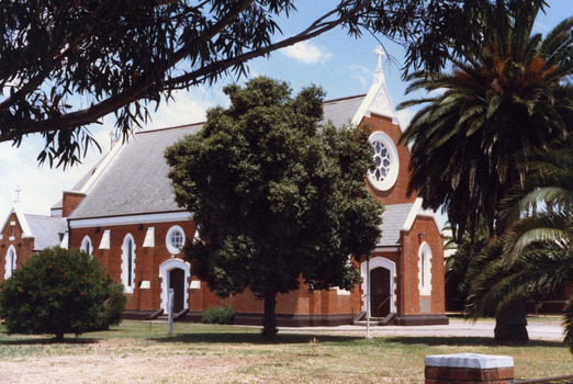 Red brick catholic church with white trim on tin roof and doors.