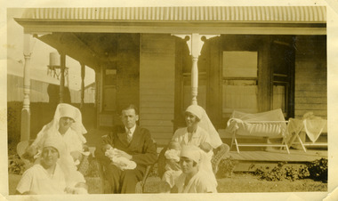 Front of bush nursing hospital with doctor, four nurses and new born in front garden. 