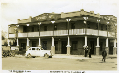 Two storey brick hotel. Veranda and deck on two sides. Cars in front and three men in front.